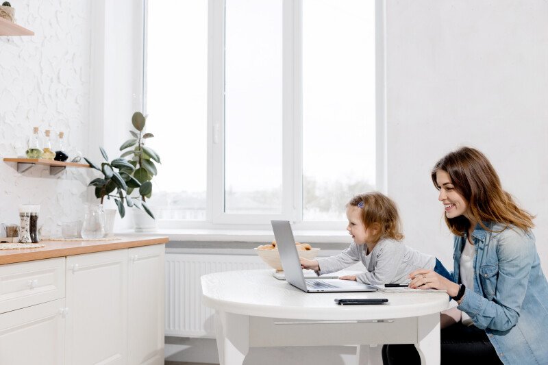 eine-frau-und-ein-kind-sitzen-an-einem-tisch-vor-einem-fenster-einer-von-ihnen-bedient-einen-laptop